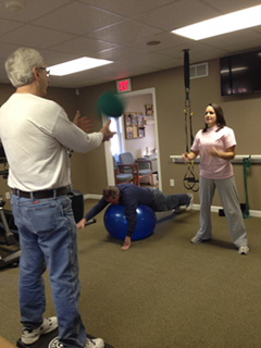 A male instructor stands and advises a young post operative patient on the proper formation of a standing exercise